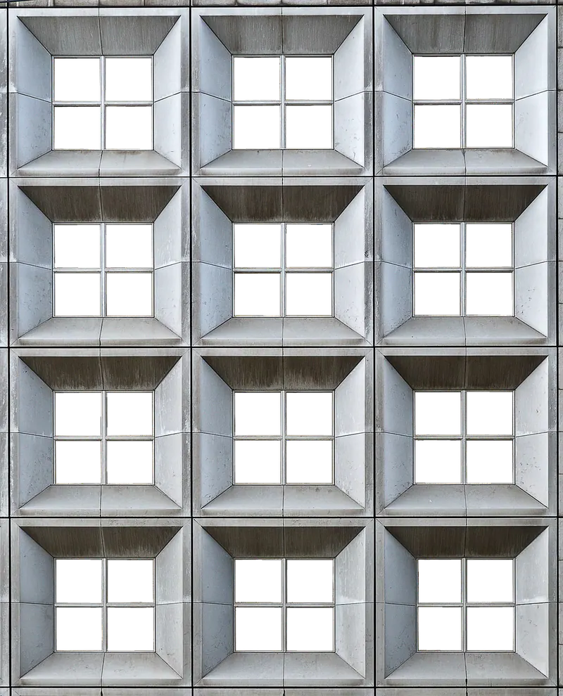Betonfassade mit gleichmäßigem Raster tiefer, schräg eingefasster Fensternischen mit vierteiligen Fenstern